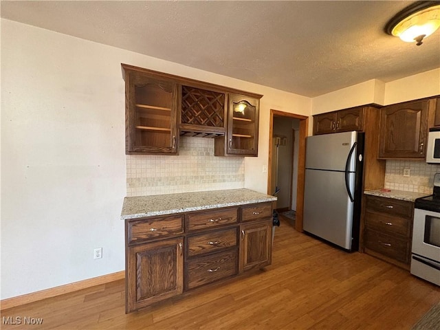 kitchen featuring dark brown cabinets, baseboards, light stone counters, appliances with stainless steel finishes, and wood finished floors