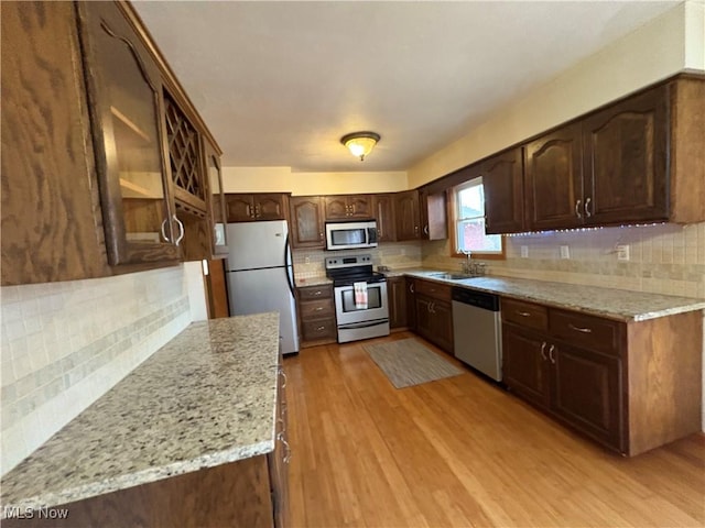 kitchen with light wood finished floors, light stone countertops, dark brown cabinetry, decorative backsplash, and stainless steel appliances