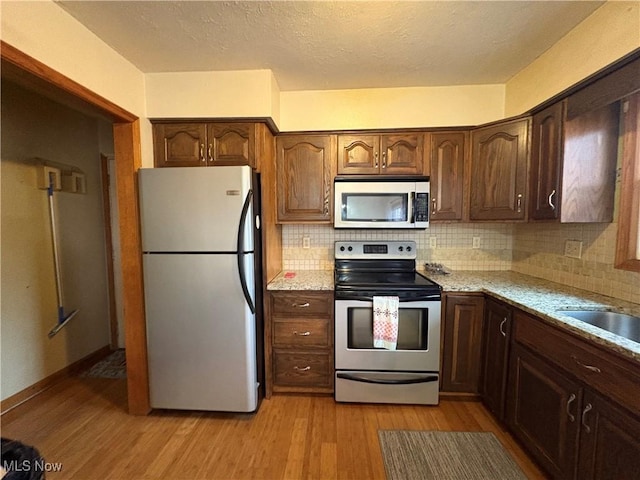 kitchen with light stone counters, stainless steel appliances, backsplash, and light wood-style flooring