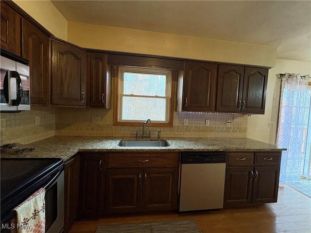 kitchen featuring backsplash, light stone countertops, dark brown cabinetry, appliances with stainless steel finishes, and a sink