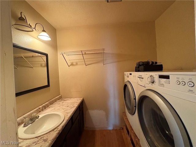 laundry room with a sink, washer and dryer, a textured ceiling, wood finished floors, and laundry area