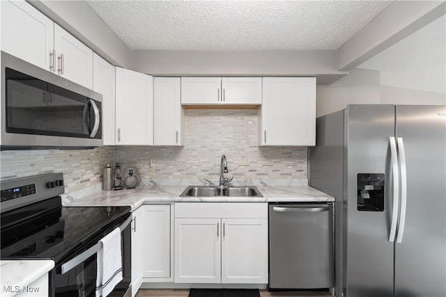 kitchen with white cabinetry, sink, light stone counters, and stainless steel appliances