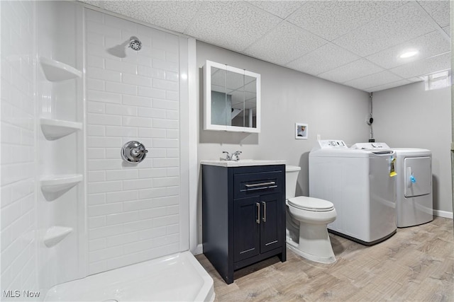 bathroom featuring tiled shower, toilet, wood-type flooring, washer and dryer, and vanity