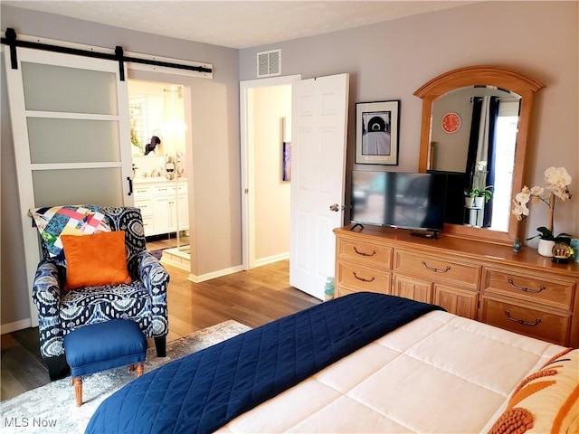 bedroom with light hardwood / wood-style floors, connected bathroom, and a barn door