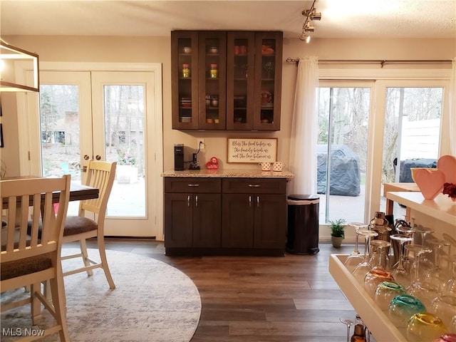 bar featuring french doors, dark brown cabinets, light stone countertops, and dark hardwood / wood-style flooring