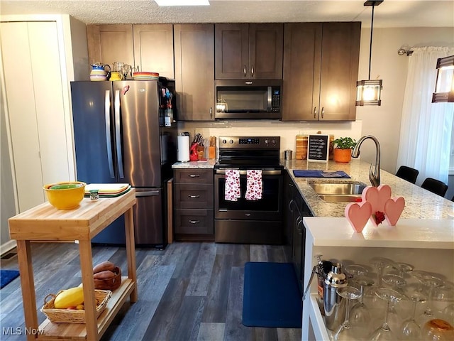 kitchen featuring appliances with stainless steel finishes, dark brown cabinets, dark wood-type flooring, decorative light fixtures, and sink