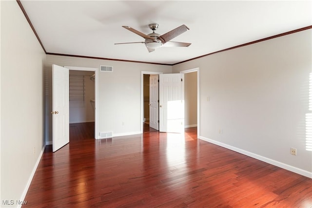 unfurnished bedroom featuring a spacious closet, ornamental molding, dark hardwood / wood-style flooring, a closet, and ceiling fan