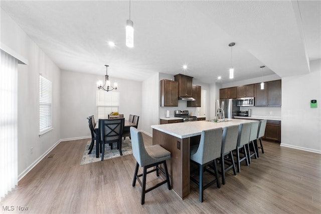 kitchen featuring dark brown cabinetry, a kitchen bar, appliances with stainless steel finishes, an island with sink, and pendant lighting