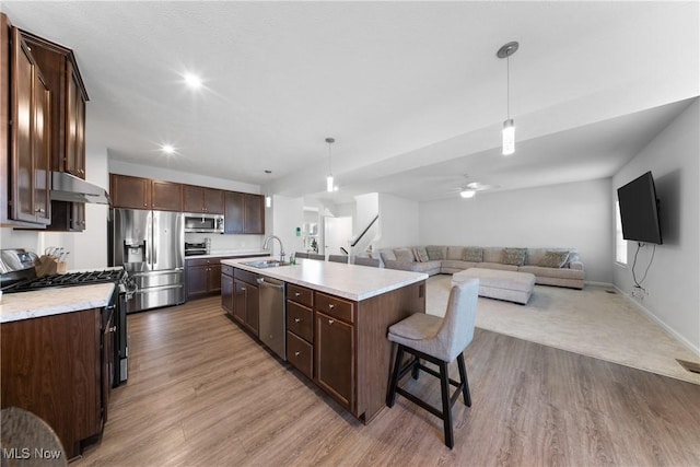 kitchen featuring appliances with stainless steel finishes, a breakfast bar, pendant lighting, sink, and a center island with sink