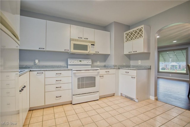 kitchen with light tile patterned floors, white cabinets, white appliances, and light stone counters