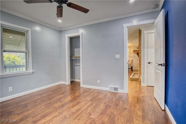 unfurnished bedroom featuring hardwood / wood-style flooring, ceiling fan, ornamental molding, a walk in closet, and a closet