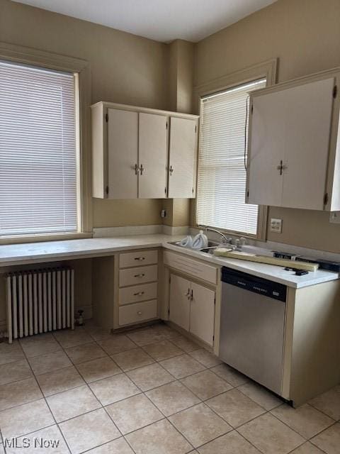 kitchen featuring radiator, built in desk, sink, stainless steel dishwasher, and light tile patterned floors