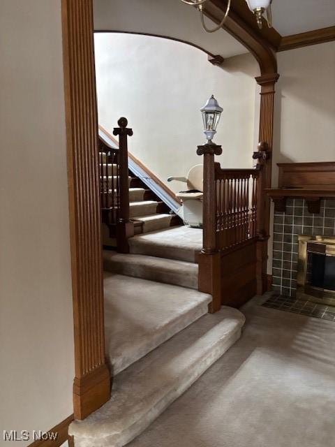 stairs featuring ornamental molding, carpet, and a fireplace