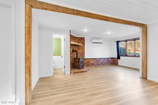 unfurnished living room featuring wood finished floors, a wood stove, baseboards, and a wall unit AC