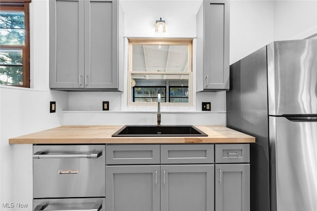 kitchen with gray cabinetry, appliances with stainless steel finishes, butcher block countertops, and a sink