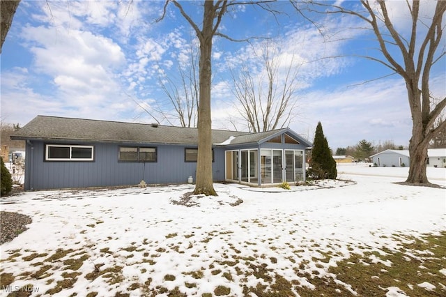 snow covered back of property with a sunroom