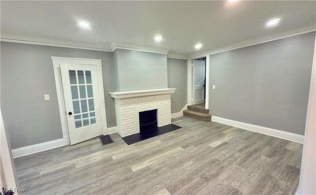 unfurnished living room with a brick fireplace, wood-type flooring, and ornamental molding