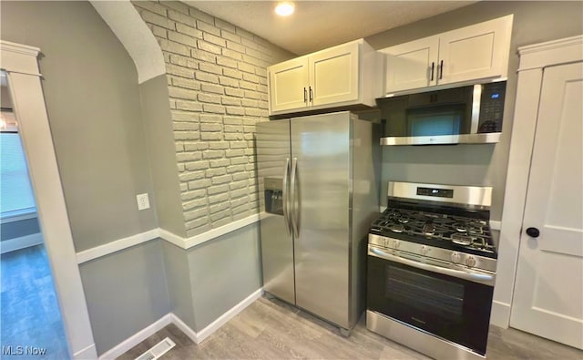 kitchen with stainless steel appliances, brick wall, white cabinets, and light hardwood / wood-style floors