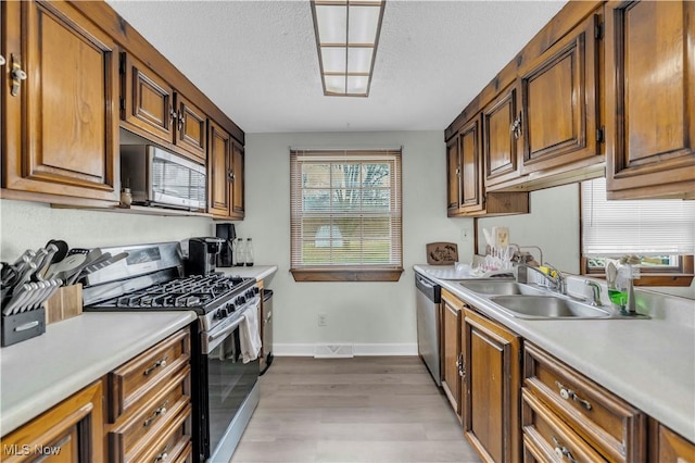 kitchen with stainless steel appliances, sink, light hardwood / wood-style floors, and a textured ceiling