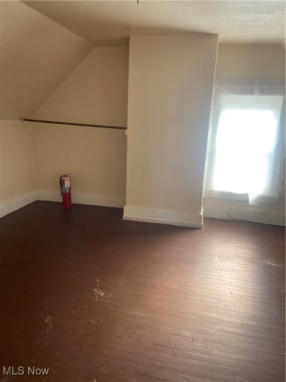 additional living space featuring dark wood-type flooring, baseboards, and vaulted ceiling
