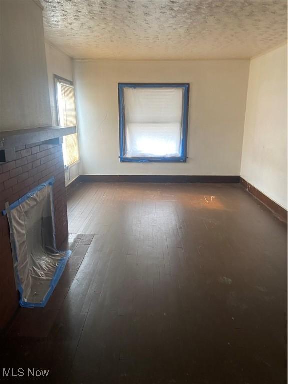 unfurnished living room with wood-type flooring, baseboards, a brick fireplace, and a textured ceiling