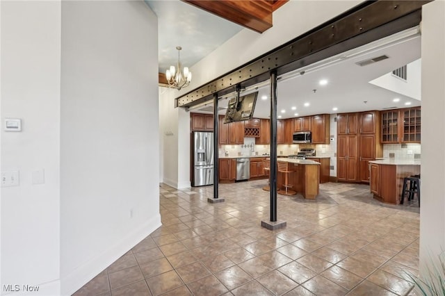 kitchen with appliances with stainless steel finishes, backsplash, a kitchen breakfast bar, a center island, and a notable chandelier