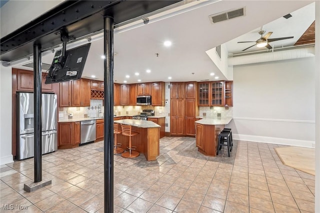 kitchen featuring a kitchen island, backsplash, a kitchen bar, ceiling fan, and stainless steel appliances