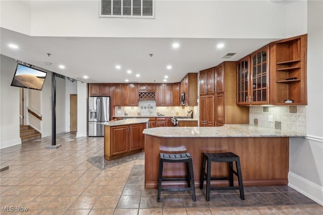 kitchen featuring a kitchen bar, decorative backsplash, kitchen peninsula, stainless steel appliances, and light stone countertops