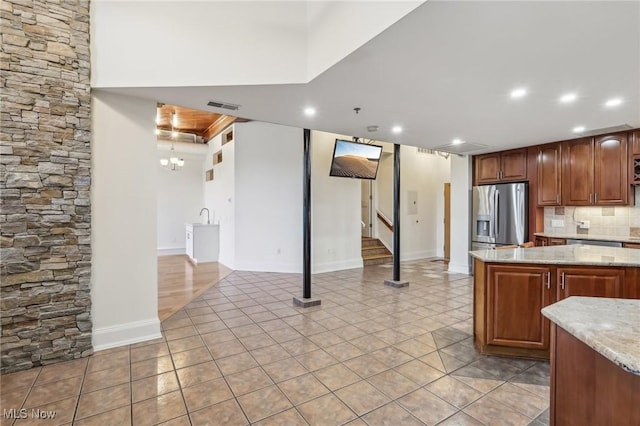 kitchen with light stone counters, light tile patterned floors, backsplash, and stainless steel refrigerator with ice dispenser