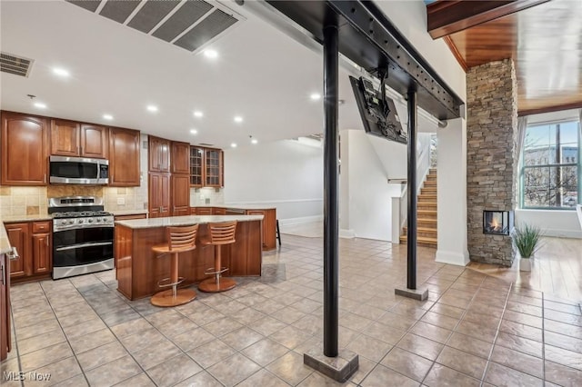 kitchen with a stone fireplace, tasteful backsplash, a kitchen breakfast bar, a center island, and stainless steel appliances