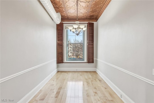 spare room featuring an inviting chandelier, crown molding, and light hardwood / wood-style flooring