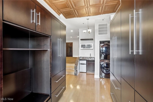 kitchen with dark brown cabinetry, stacked washer and clothes dryer, decorative light fixtures, and light wood-type flooring