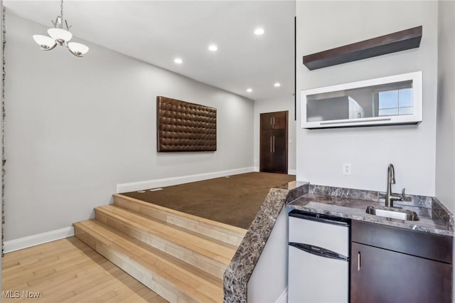 kitchen featuring sink, light wood-type flooring, stainless steel refrigerator, a notable chandelier, and pendant lighting