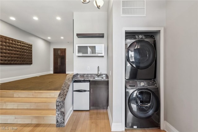 laundry room with stacked washer and dryer, sink, and light hardwood / wood-style floors