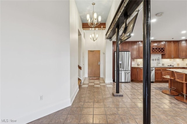 kitchen with tile patterned floors, a chandelier, hanging light fixtures, appliances with stainless steel finishes, and decorative backsplash