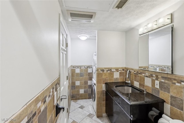 bathroom featuring stacked washing maching and dryer, tile walls, vanity, and a textured ceiling