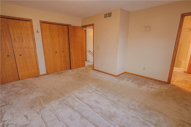 unfurnished bedroom featuring light carpet and two closets