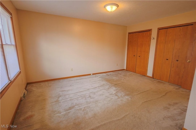 unfurnished bedroom featuring light colored carpet and multiple closets