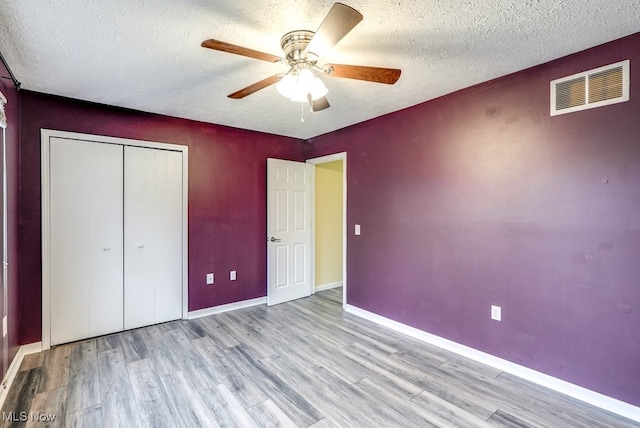 unfurnished bedroom with ceiling fan, a closet, a textured ceiling, and light wood-type flooring