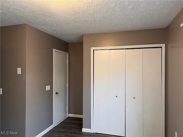 unfurnished bedroom with dark hardwood / wood-style floors, a textured ceiling, and a closet