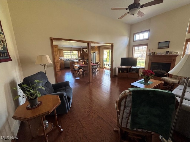 living room featuring ceiling fan, a towering ceiling, dark hardwood / wood-style floors, and a healthy amount of sunlight