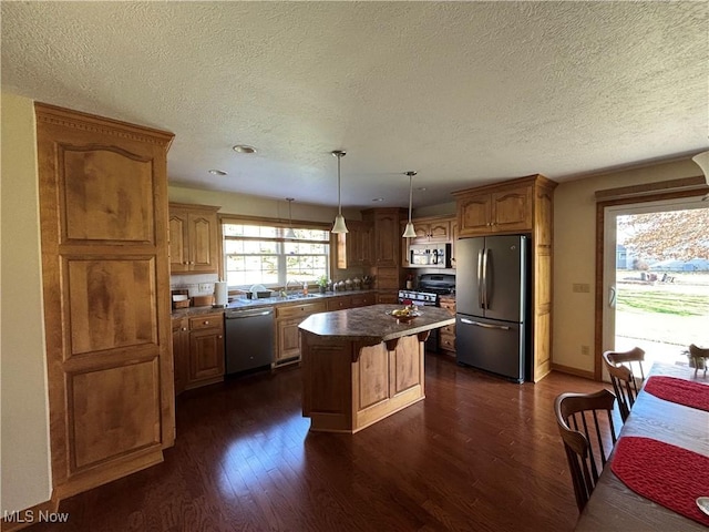 kitchen with stainless steel appliances, a kitchen island, dark wood-type flooring, and hanging light fixtures