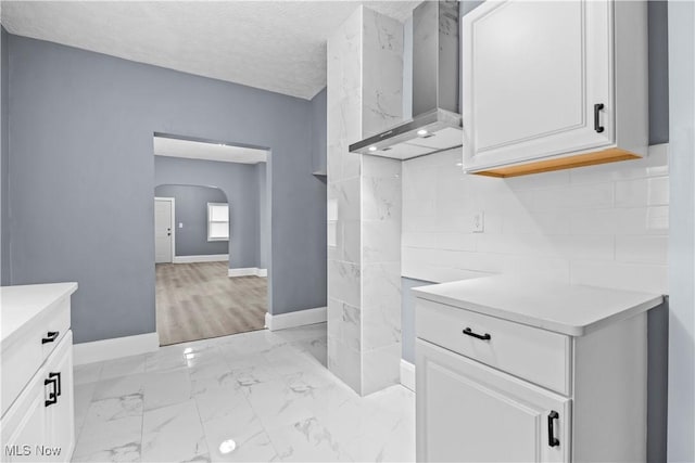 kitchen with backsplash, wall chimney range hood, white cabinets, and a textured ceiling