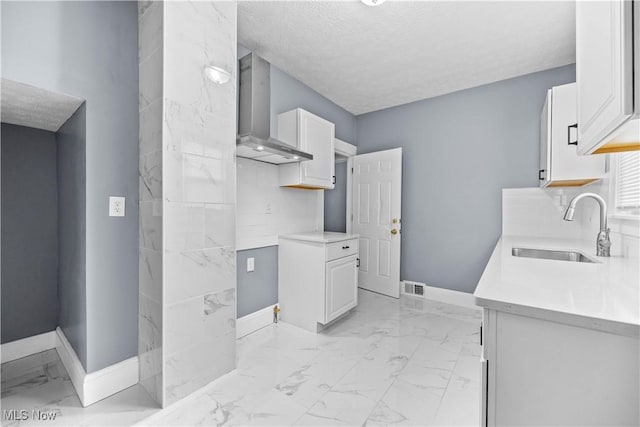 kitchen featuring white cabinetry, wall chimney exhaust hood, sink, and a textured ceiling