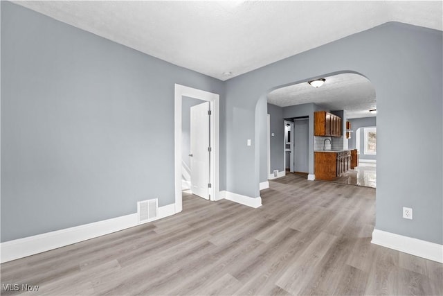 unfurnished living room with sink, a textured ceiling, and light wood-type flooring