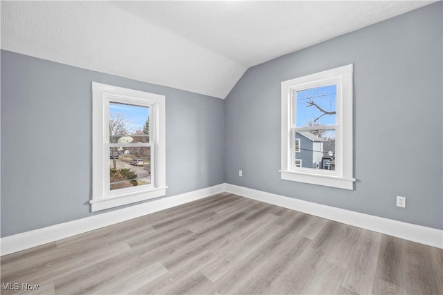 bonus room with plenty of natural light, vaulted ceiling, and light wood-type flooring