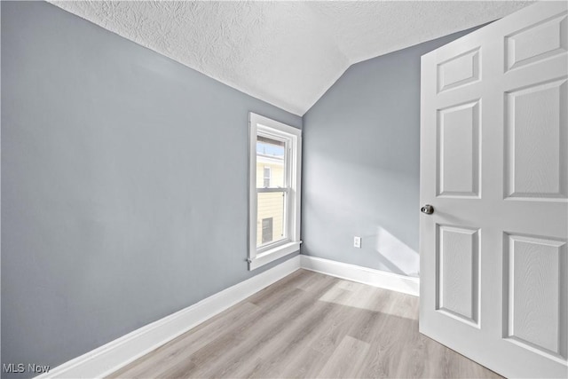 spare room featuring light hardwood / wood-style flooring, vaulted ceiling, and a textured ceiling