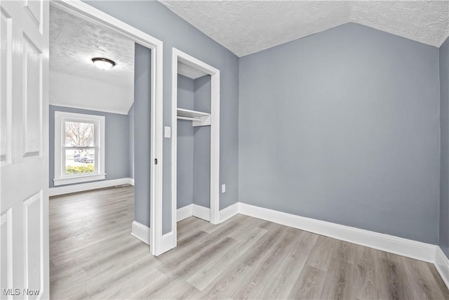 unfurnished bedroom featuring a closet, lofted ceiling, a textured ceiling, and light hardwood / wood-style flooring