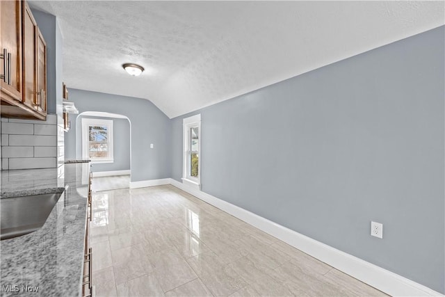 unfurnished dining area featuring plenty of natural light, sink, vaulted ceiling, and a textured ceiling