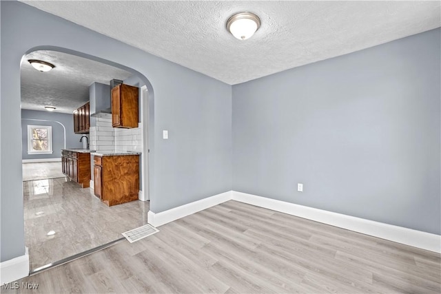 spare room with sink, light hardwood / wood-style flooring, and a textured ceiling